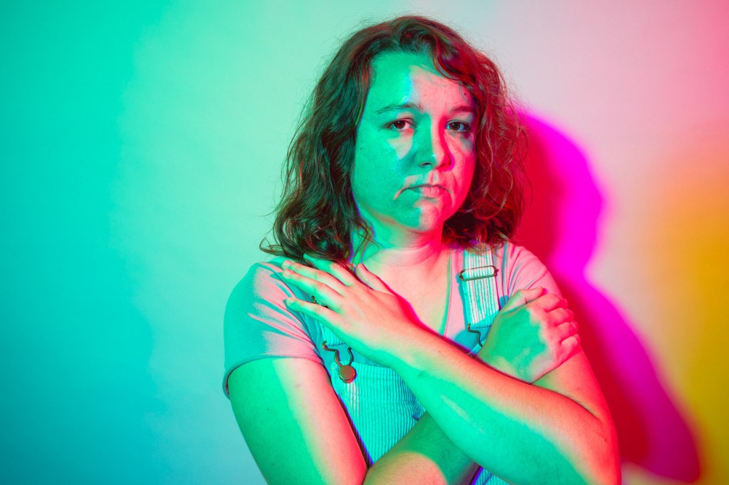 Meghan with arms crossed, lit in teal and pink studio light