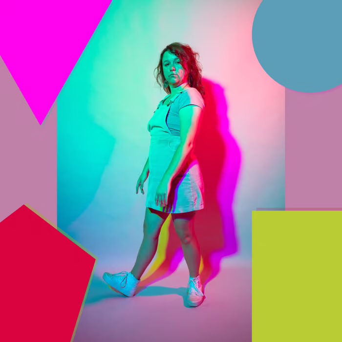 Meghan standing among bright geometric shapes in pink, teal, and chartreuse light